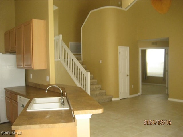 kitchen with kitchen peninsula, light brown cabinetry, dishwasher, sink, and a high ceiling