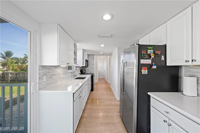 kitchen with tasteful backsplash, black range with electric stovetop, stainless steel fridge, and white cabinets