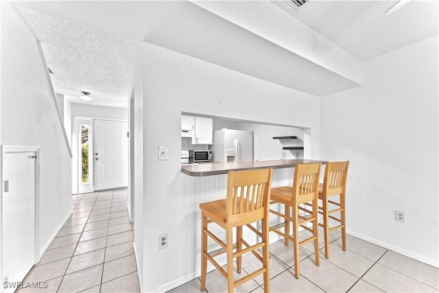 kitchen with a kitchen breakfast bar, a textured ceiling, light tile patterned floors, white cabinets, and white fridge with ice dispenser