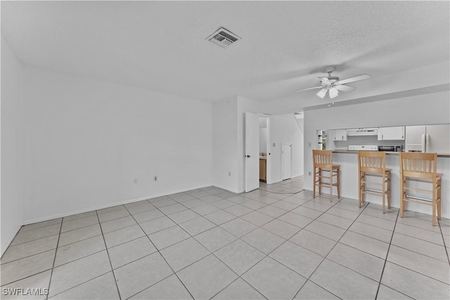 unfurnished living room featuring ceiling fan, light tile patterned floors, and a textured ceiling