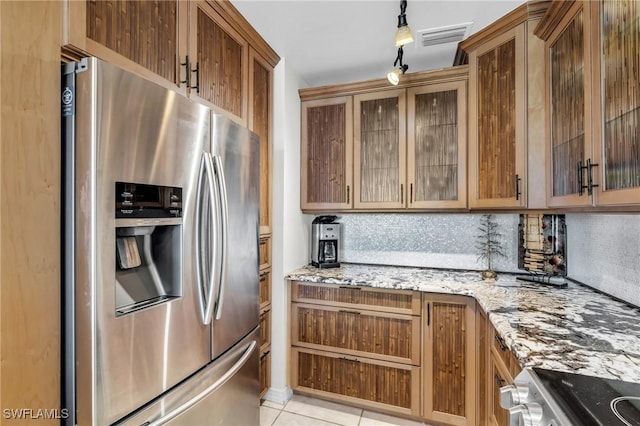 kitchen featuring decorative backsplash, rail lighting, stainless steel fridge with ice dispenser, light tile patterned flooring, and light stone counters