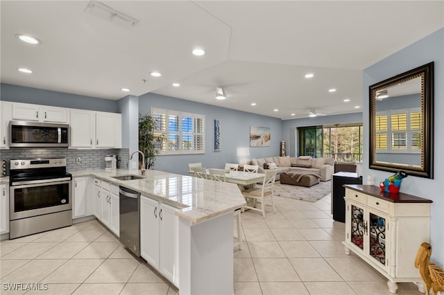 kitchen with light stone countertops, white cabinetry, sink, stainless steel appliances, and kitchen peninsula