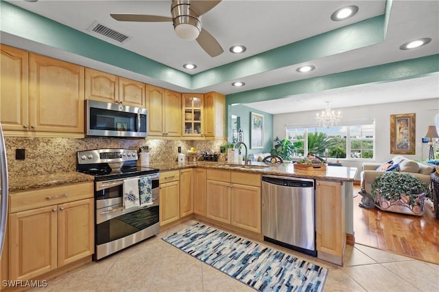 kitchen with appliances with stainless steel finishes, light stone counters, ceiling fan with notable chandelier, sink, and light tile patterned floors