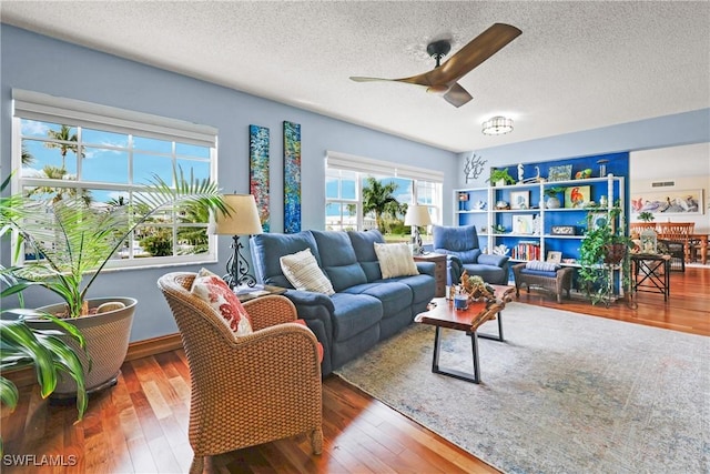 living room with a textured ceiling, ceiling fan, and dark wood-type flooring