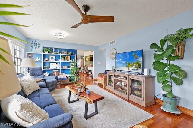 living room with built in shelves, ceiling fan, wood-type flooring, and a textured ceiling