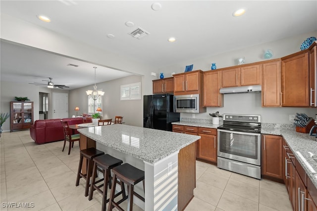 kitchen featuring light stone countertops, pendant lighting, a kitchen island, ceiling fan with notable chandelier, and appliances with stainless steel finishes