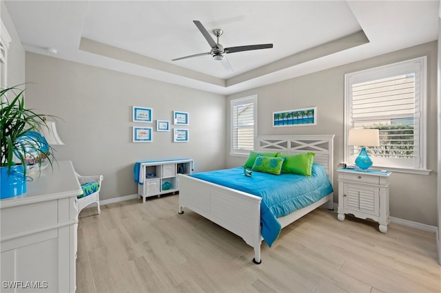 bedroom with a raised ceiling, ceiling fan, and light hardwood / wood-style flooring