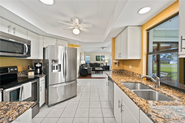 kitchen with a raised ceiling, sink, ceiling fan, appliances with stainless steel finishes, and white cabinetry