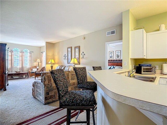 kitchen featuring a kitchen bar, kitchen peninsula, light colored carpet, sink, and white cabinetry