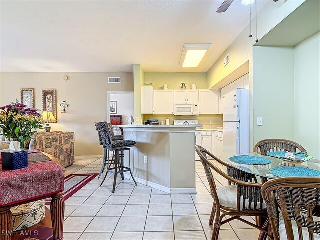 kitchen featuring a kitchen bar, kitchen peninsula, white appliances, light tile patterned floors, and white cabinetry