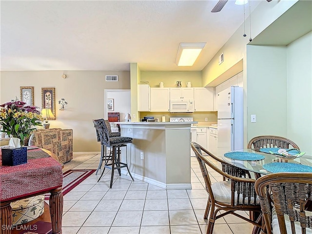 kitchen with light tile patterned flooring, a breakfast bar area, white cabinets, kitchen peninsula, and white appliances