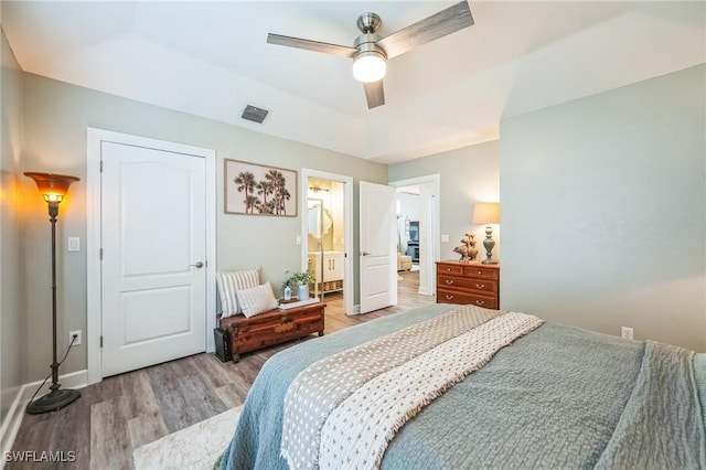 bedroom with light hardwood / wood-style flooring, ensuite bath, ceiling fan, and a tray ceiling