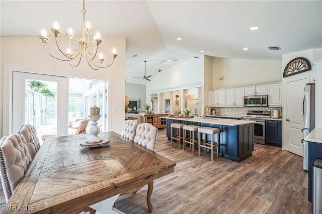 dining area with wood-type flooring, ceiling fan with notable chandelier, high vaulted ceiling, and sink