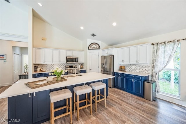 kitchen featuring decorative backsplash, appliances with stainless steel finishes, blue cabinetry, white cabinets, and an island with sink