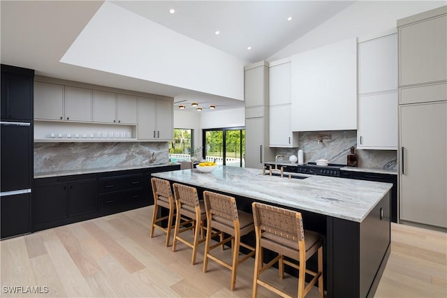 kitchen featuring light stone counters, a sink, light wood-style flooring, and a kitchen bar