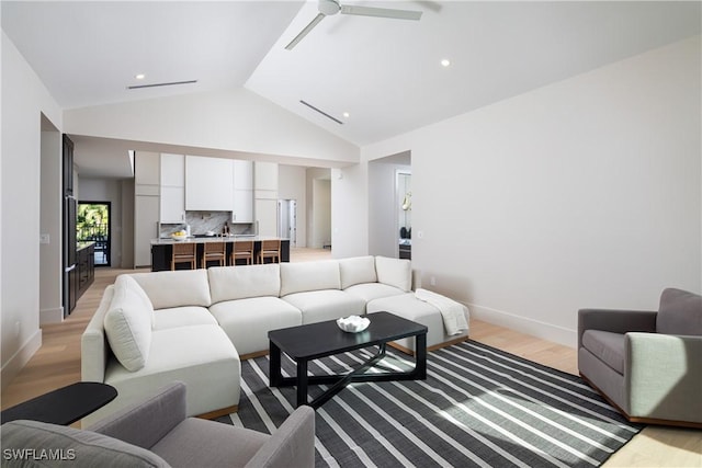 living room featuring a ceiling fan, high vaulted ceiling, light wood-style flooring, and baseboards