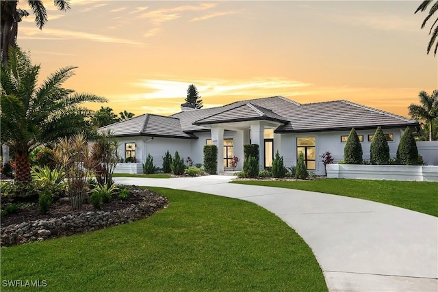 prairie-style home with driveway, a tiled roof, a front lawn, and stucco siding