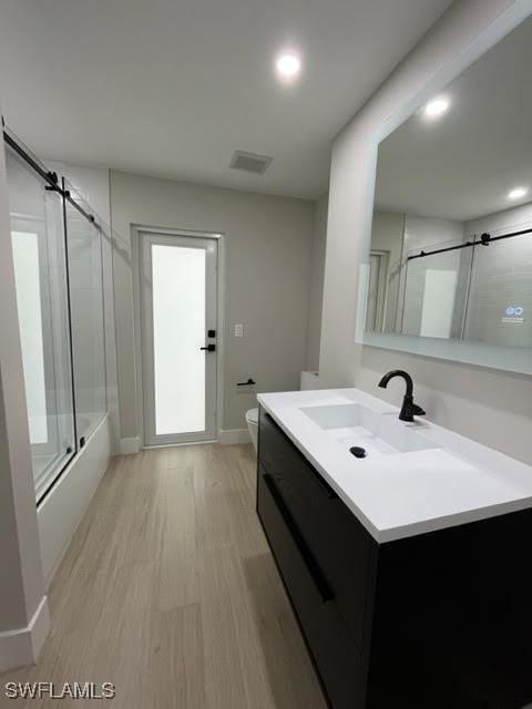 full bathroom with hardwood / wood-style floors, vanity, toilet, enclosed tub / shower combo, and plenty of natural light