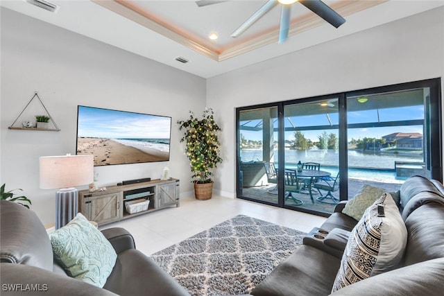 living room featuring ceiling fan, a raised ceiling, ornamental molding, and light tile patterned floors