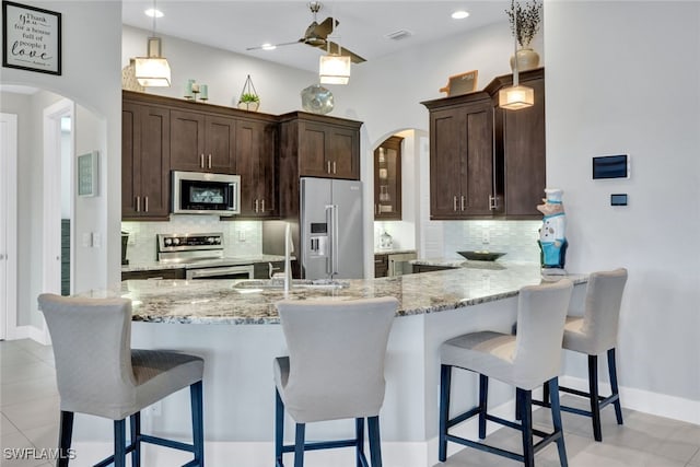 kitchen featuring light stone counters, kitchen peninsula, stainless steel appliances, and tasteful backsplash