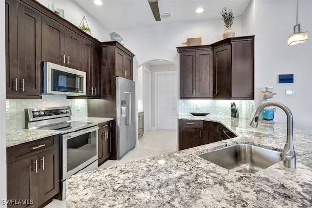 kitchen with light stone counters, sink, stainless steel appliances, and hanging light fixtures