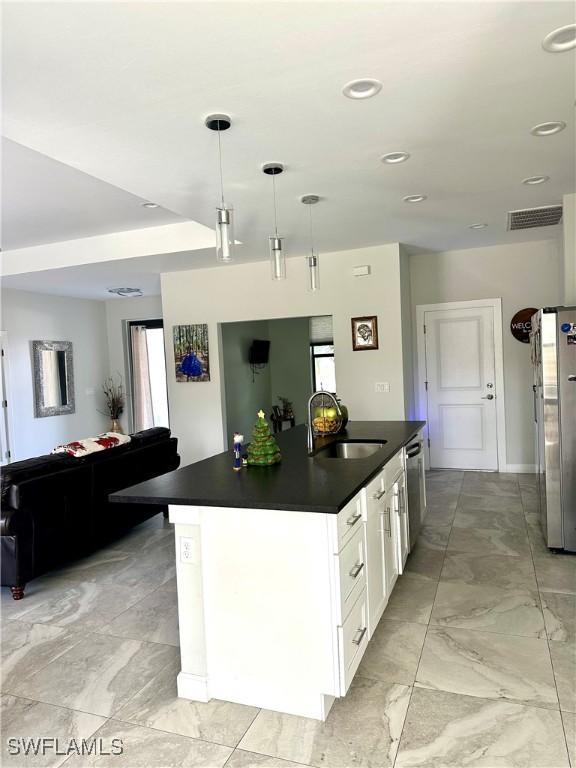 kitchen with pendant lighting, white cabinets, a center island with sink, sink, and appliances with stainless steel finishes