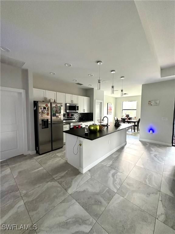 kitchen with stainless steel appliances, sink, pendant lighting, white cabinetry, and an island with sink