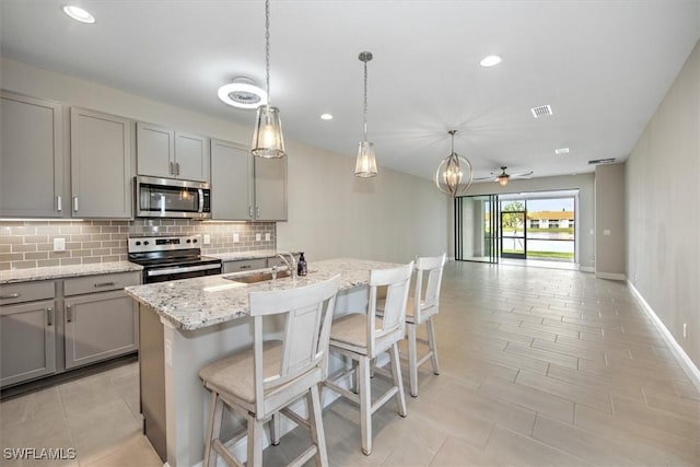 kitchen with sink, appliances with stainless steel finishes, gray cabinetry, and a kitchen island with sink