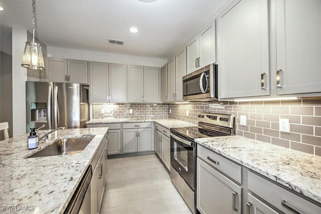 kitchen with light stone countertops, appliances with stainless steel finishes, decorative light fixtures, sink, and gray cabinets