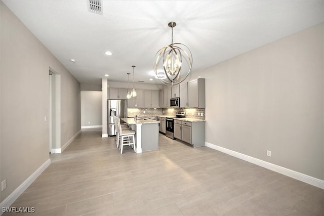 kitchen featuring appliances with stainless steel finishes, a kitchen bar, decorative light fixtures, gray cabinets, and a kitchen island with sink