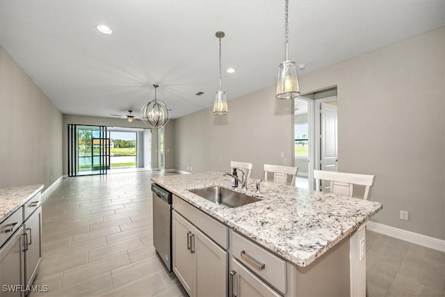 kitchen featuring decorative light fixtures, a center island with sink, stainless steel dishwasher, sink, and light stone counters