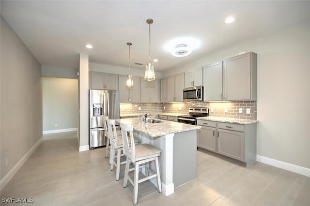 kitchen featuring stainless steel appliances, an island with sink, sink, a kitchen breakfast bar, and light stone counters