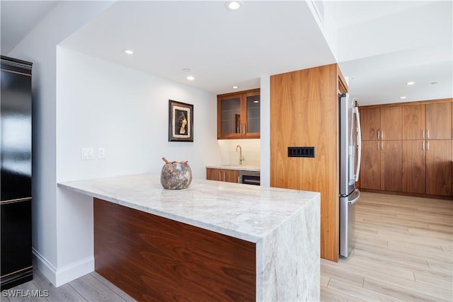 kitchen featuring sink, stainless steel fridge, light stone counters, kitchen peninsula, and light hardwood / wood-style flooring