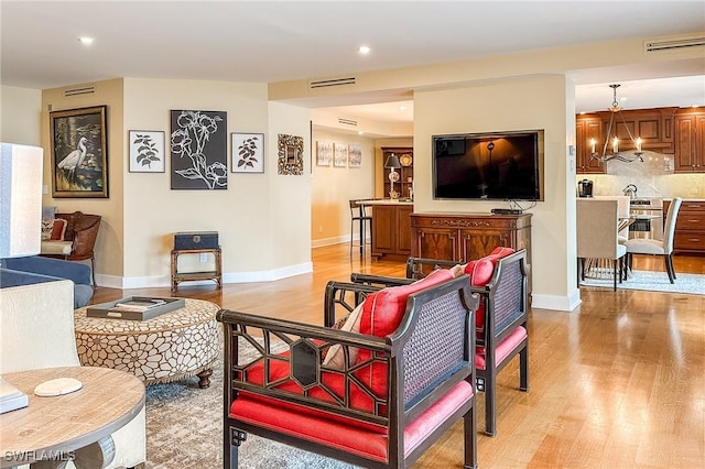 living area featuring visible vents, baseboards, light wood-type flooring, and an inviting chandelier