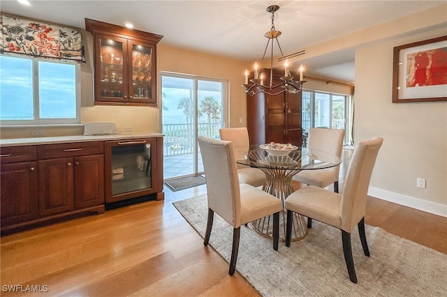 dining space with wine cooler, baseboards, a chandelier, and light wood finished floors