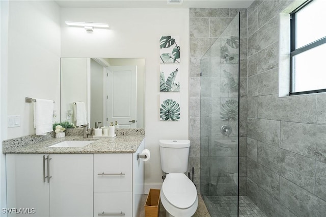 bathroom with a tile shower, vanity, a healthy amount of sunlight, and toilet