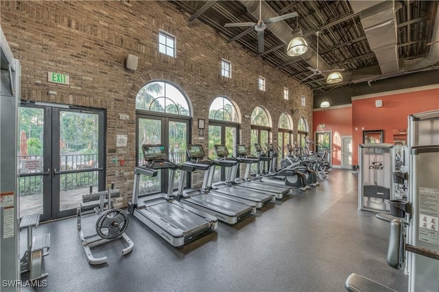 exercise room featuring ceiling fan, french doors, brick wall, and a high ceiling