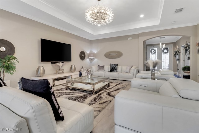 living room with crown molding, light hardwood / wood-style flooring, a raised ceiling, and a chandelier