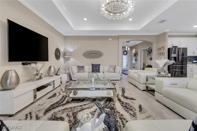 living room with a raised ceiling, an inviting chandelier, and crown molding