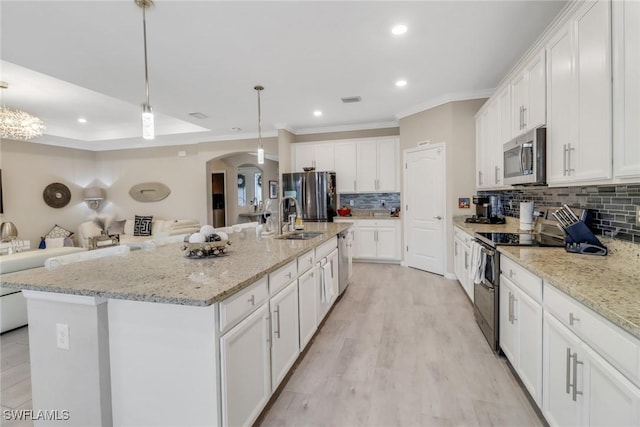 kitchen with decorative light fixtures, a kitchen island with sink, white cabinetry, and appliances with stainless steel finishes