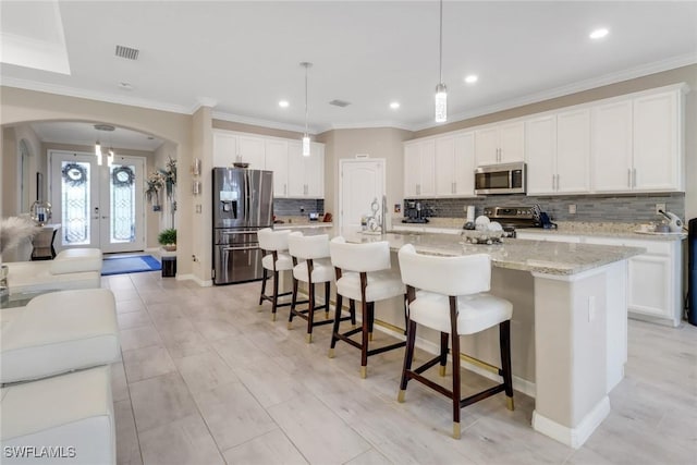 kitchen featuring hanging light fixtures, white cabinets, stainless steel appliances, and a kitchen island with sink