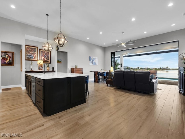 kitchen with light wood-type flooring, light stone counters, ceiling fan, sink, and pendant lighting