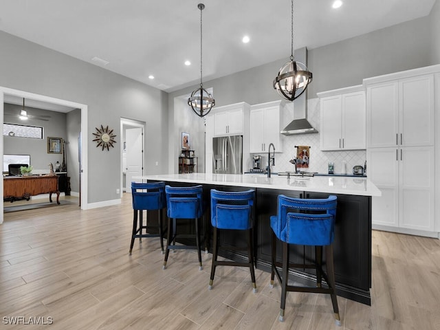 kitchen with a kitchen breakfast bar, wall chimney exhaust hood, a spacious island, decorative light fixtures, and stainless steel fridge with ice dispenser