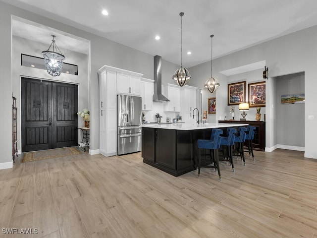 kitchen with stainless steel refrigerator with ice dispenser, decorative light fixtures, white cabinetry, and wall chimney exhaust hood