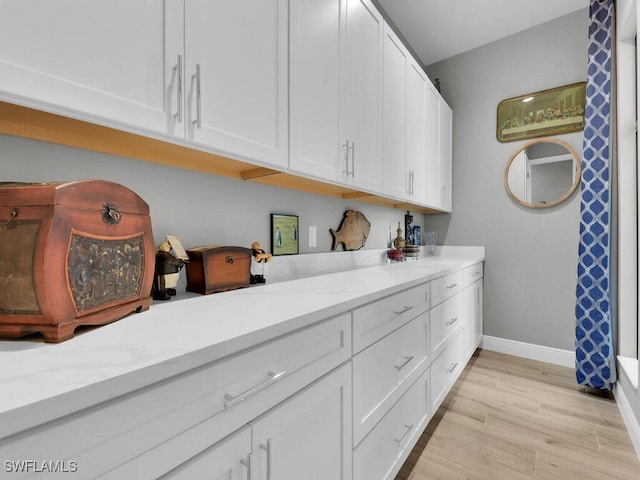 kitchen featuring white cabinets, light wood-type flooring, and light stone counters