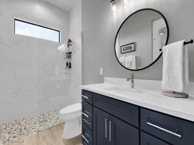 bathroom featuring tiled shower, vanity, wood-type flooring, and toilet