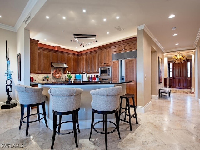 kitchen with backsplash, a kitchen breakfast bar, crown molding, built in appliances, and a notable chandelier