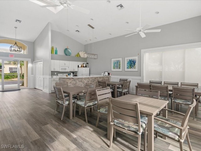 dining area with hardwood / wood-style floors, ceiling fan, high vaulted ceiling, and a skylight