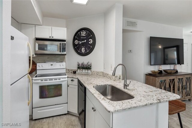 kitchen with kitchen peninsula, sink, white cabinets, light stone counters, and white appliances