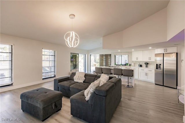 living room featuring a chandelier, sink, high vaulted ceiling, and light hardwood / wood-style floors